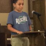 Young boy giving an LTC speech at a church lectern while wearing a “Rescued” T-shirt.