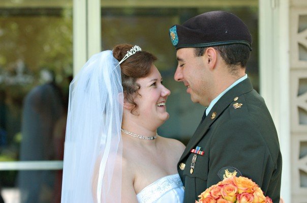 Angie and Peter smiling at each other on their wedding day, with Peter in his Army dress uniform and Angie wearing her wedding gown and veil