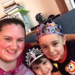 A mom wearing her wedding tiara poses with her young daughter in a dress-up tiara and her young son wearing a homemade paper crown