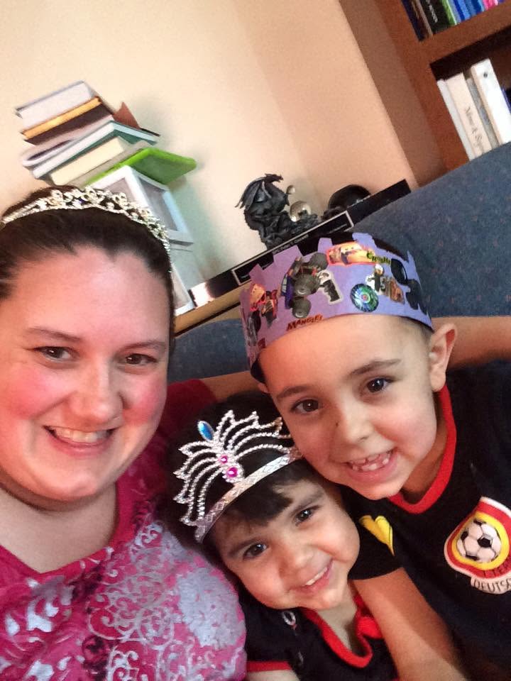 A mom wearing her wedding tiara poses with her young daughter in a dress-up tiara and her young son wearing a homemade paper crown