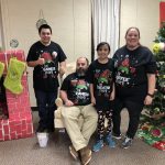 amily of four wearing matching Christmas gnome shirts beside a Grinch-themed Christmas tree and fireplace.