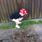 Young boy crouching down to examine something among the flowers beside a wooden building