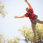 Dietrich wearing a safety harness during the Leap of Faith high-ropes activity at summer camp, reaching outward as he leaps from the platform.