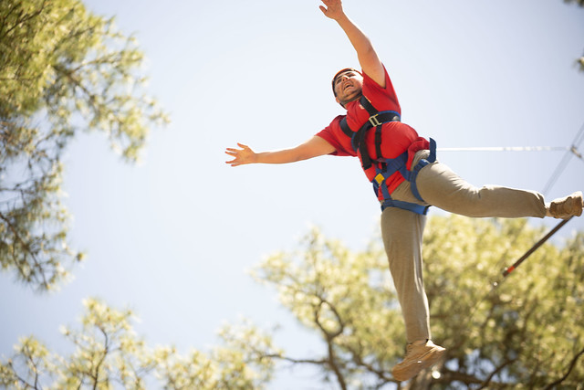 Dietrich wearing a safety harness during the Leap of Faith high-ropes activity at summer camp, reaching outward as he leaps from the platform.