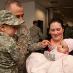 A father in Army uniform reunites with his wife and two young children at a military homecoming