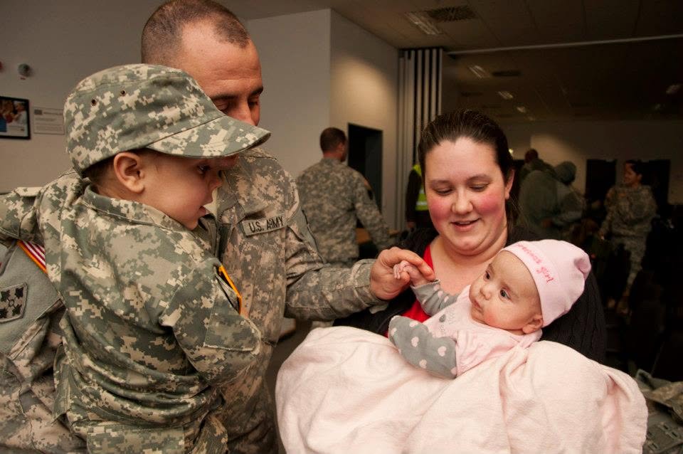A father in Army uniform reunites with his wife and two young children at a military homecoming