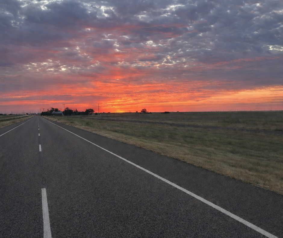 Straight two-lane road extending toward the horizon beneath a colorful sunset sky.