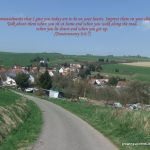 Winding road descending toward a German village surrounded by rolling green fields