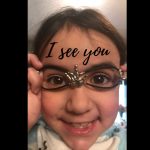 Close-up photo of a child looking toward the camera while holding novelty glasses, with the words “I see you” written across the image.