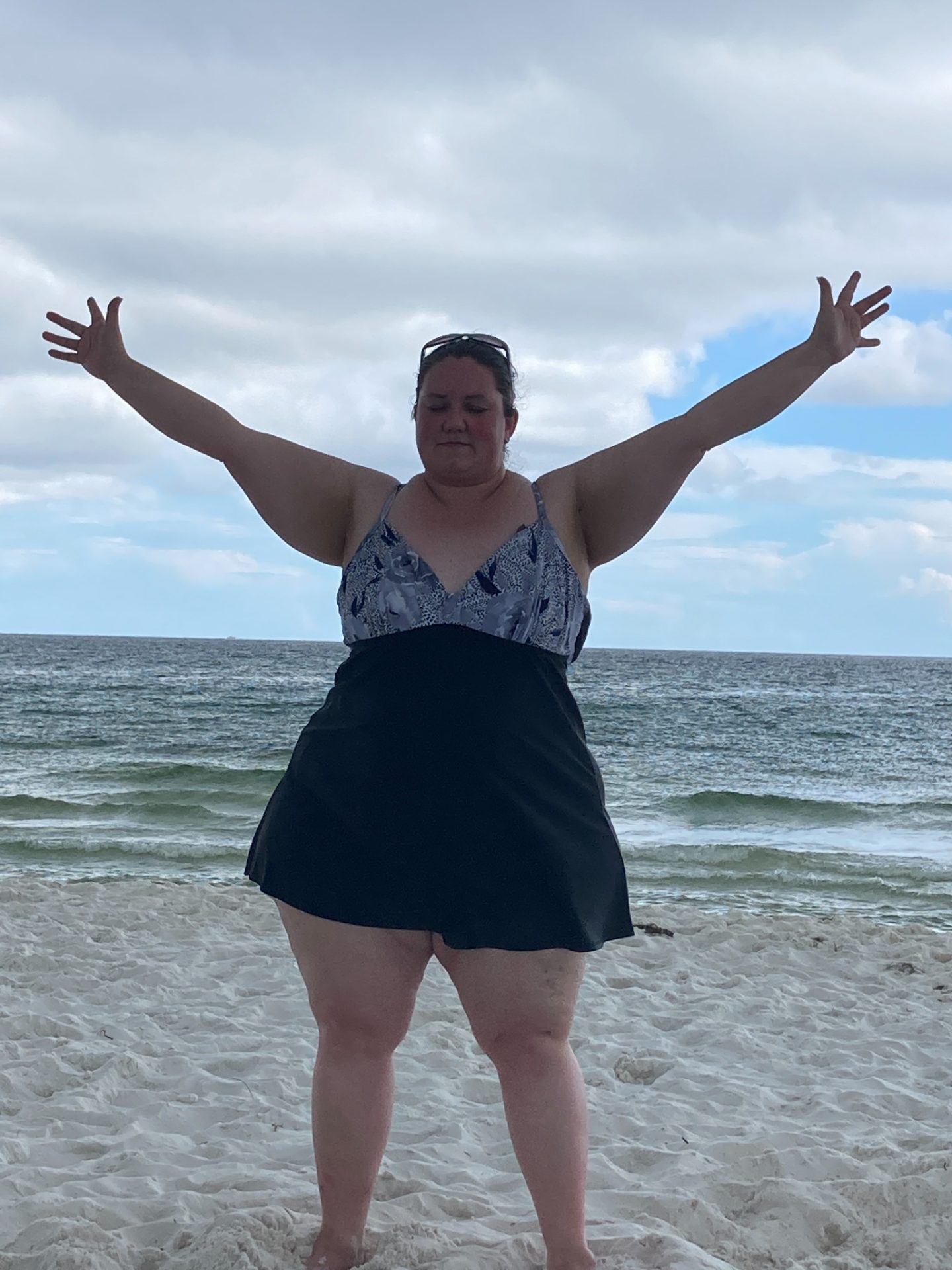 Woman standing on the beach with arms outstretched in front of the ocean