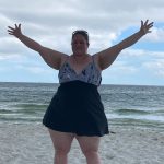 Woman standing on the beach with arms outstretched in front of the ocean