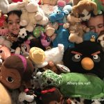 Two children hide beneath a large pile of stuffed animals with the words “Where are we?”