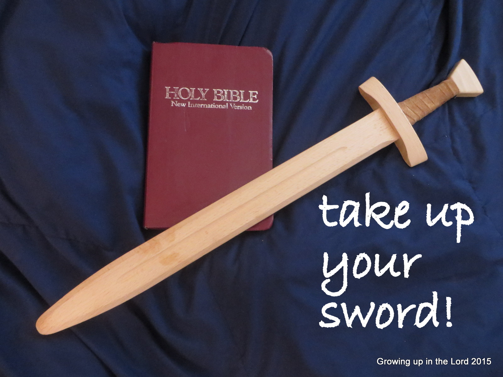 A wooden sword lies across a Bible with the words “take up your sword!”