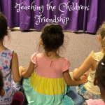 Young children sit together holding hands during a Bible class puppet show.