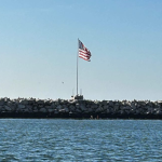 American flag flying above a rocky shoreline with the words