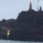 People jumping from a rocky shoreline into the ocean in Hawaii.