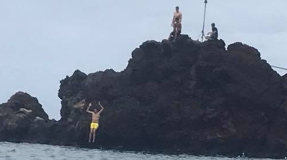 People jumping from a rocky shoreline into the ocean in Hawaii.
