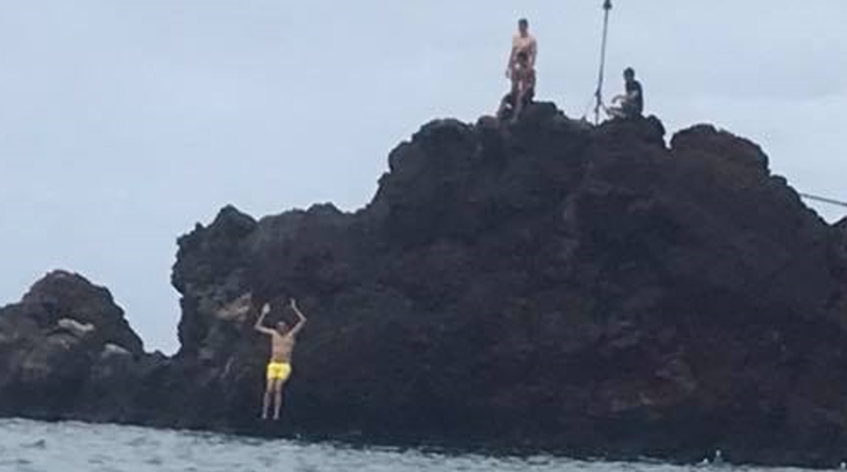 People jumping from a rocky shoreline into the ocean in Hawaii.