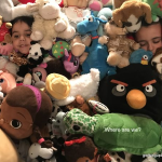 Two children lying in a pile of stuffed animals, almost completely hidden among the colorful toys