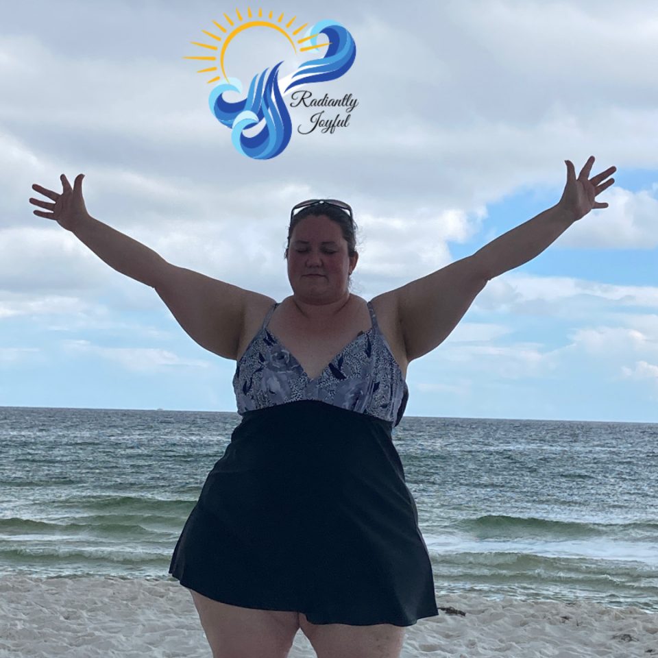 Woman standing on the beach with arms outstretched in front of the ocean.
