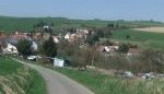 Winding road descending toward a German village surrounded by rolling green fields.